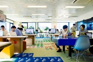 「チームラボ本社」チームラボの本社オフィス@東京。チームラボのオフィスはオフィス全体がディズニーランドみたいに楽しい空間になることを目指しました。オフィスのあちこちに、制作したアートやプロダクトを展示しています。床は木のパーツ集めた森や、花のパーツを集めた花畑、波のパーツを集めた海など、ドラクエのマップをヒントに森や海やビーチがある世界をつくることで、作品を見て回りながら森から海、海から花畑を巡って世界を冒険できるようにしています。その時になりたい気分に応じて、花畑や海で会議が行われます。