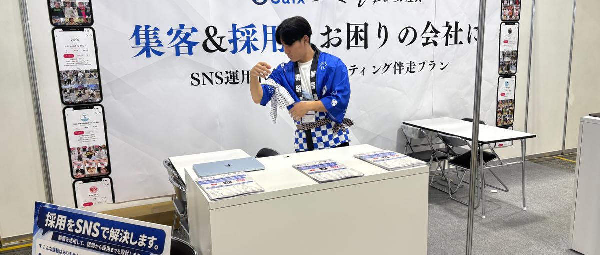 AI展示会のブースで、来場した経営者に声をかける営業スタッフ
